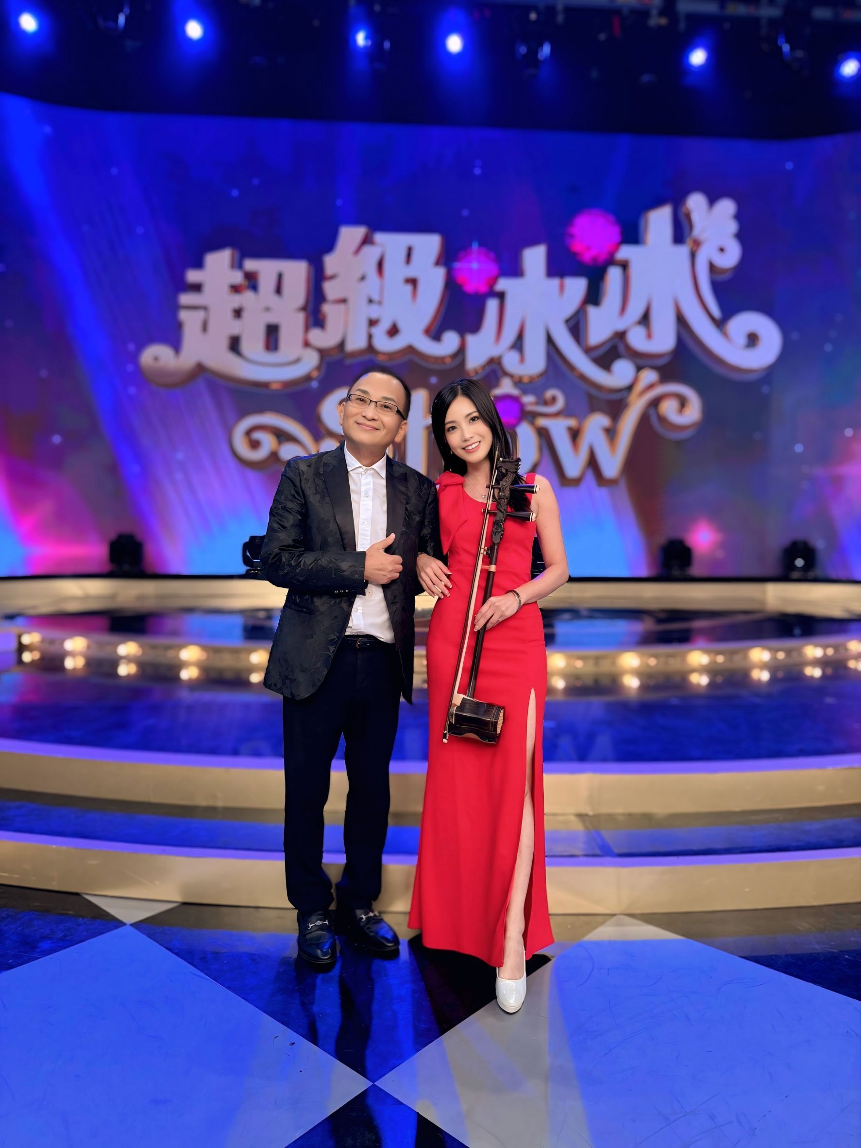 胡琴姐姐身穿紅色禮服手持二胡，於《超級冰冰Show》舞台前合影